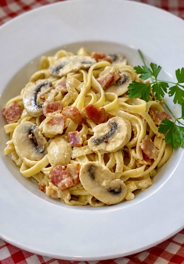 Portrait image of Fettuccine Boscaiola with crispy bacon, sautéed mushrooms and creamy sauce, garnished with fresh parsley