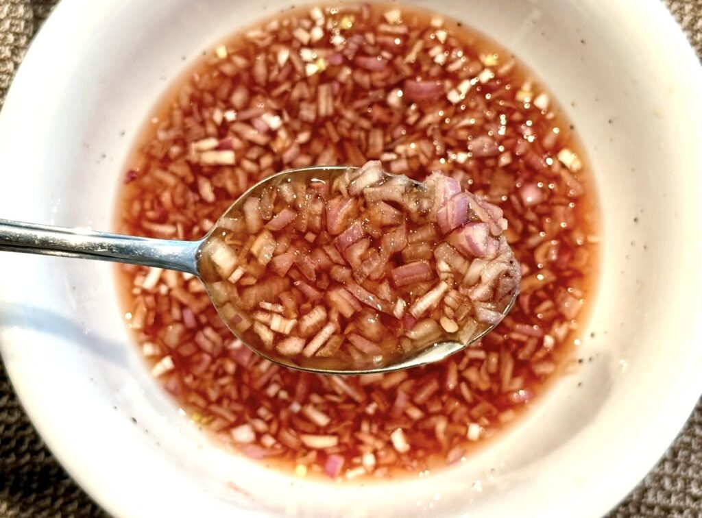 Mignonette Sauce For Oysters shown close-up with red wine vinegar and shallots mixed together