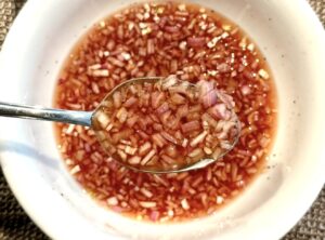 Mignonette Sauce For Oysters shown close-up with red wine vinegar and shallots mixed together
