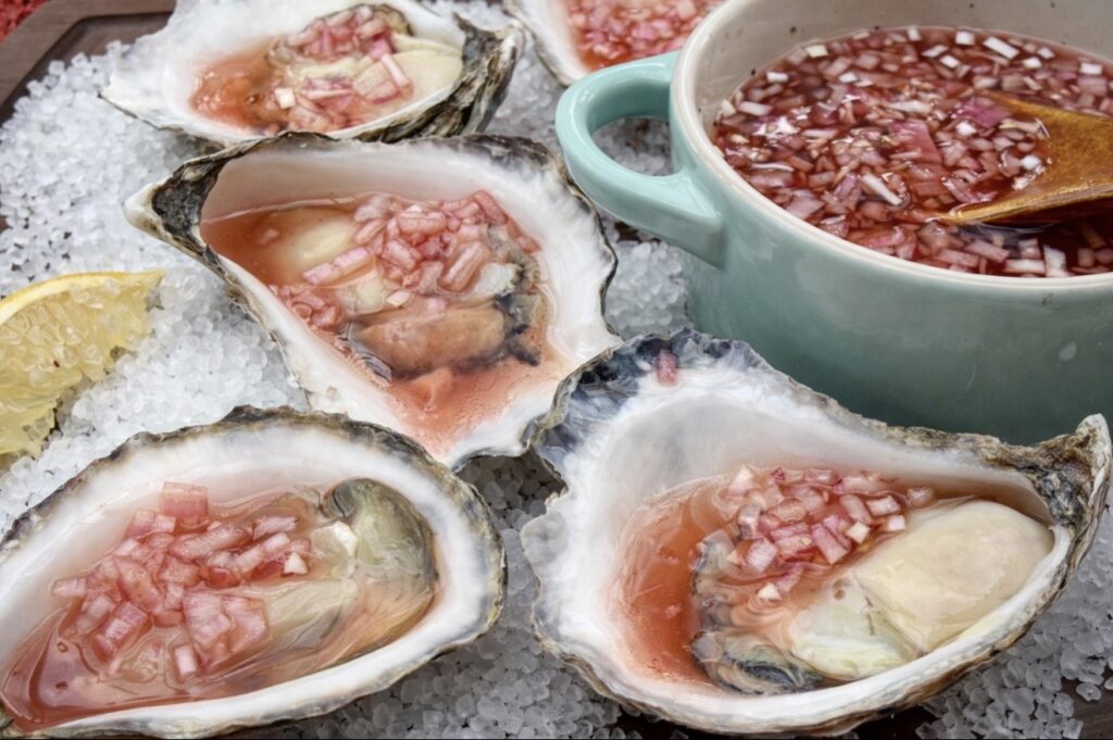 Mignonette Sauce For Oysters served in a small bowl next to raw oysters displayed on rock salt