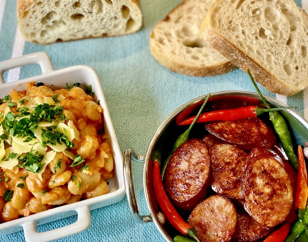 Creamy butter beans topped with parsley and shaved cheese served beside pan fried chorizo with red and green chillies and crusty bread.