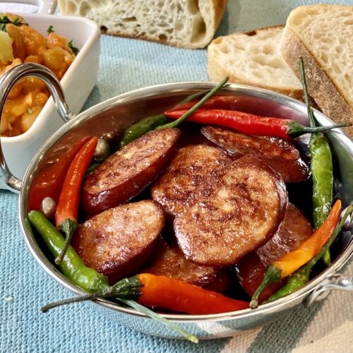 Pan fried chorizo slices with red and green chillies in a small metal serving bowl.
