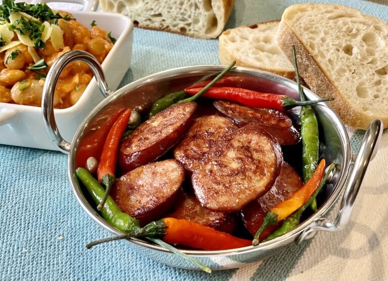 Pan fried chorizo slices with red and green chillies in a small metal serving bowl.