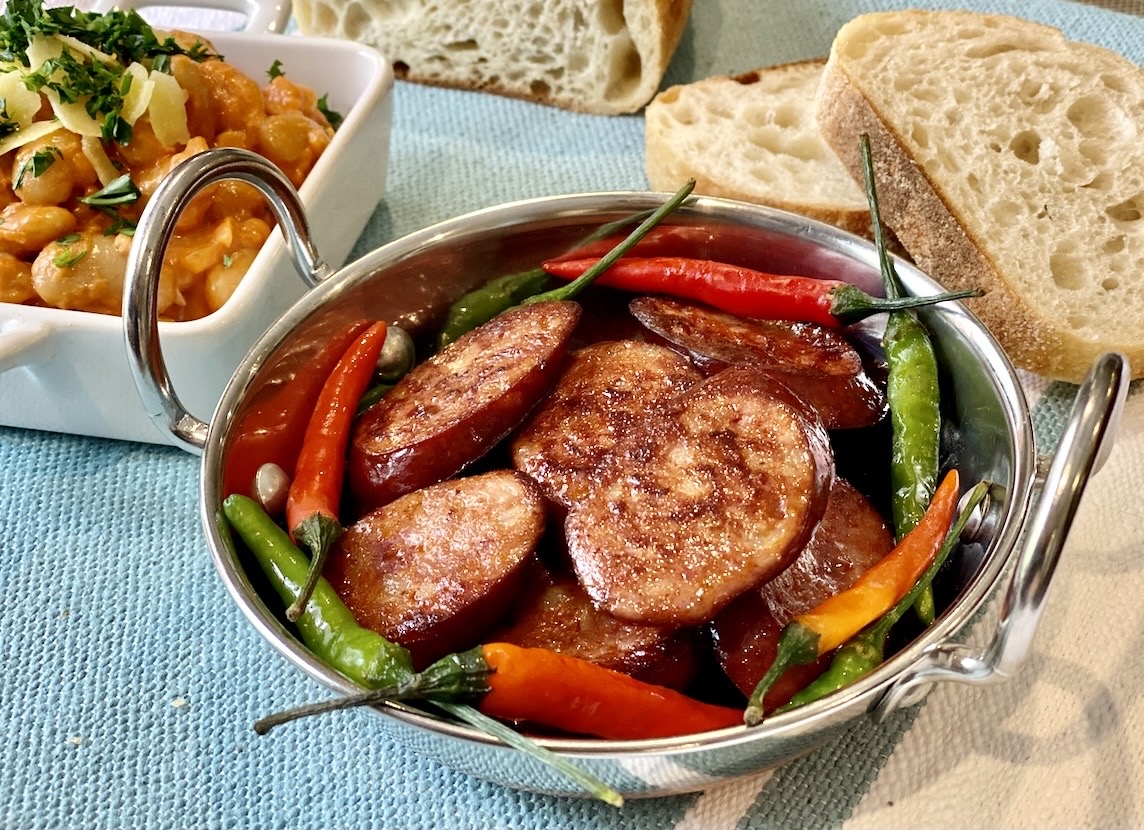 Pan fried chorizo slices with red and green chillies in a small metal serving bowl.