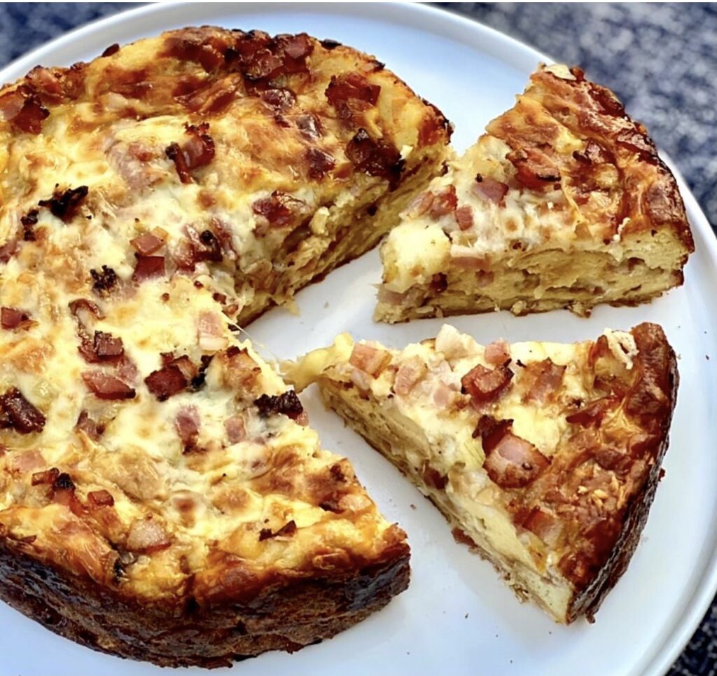 Sliced overnight strata with eggs bacon and cheese, showing a soft layered interior with melted cheese and crispy bacon throughout.