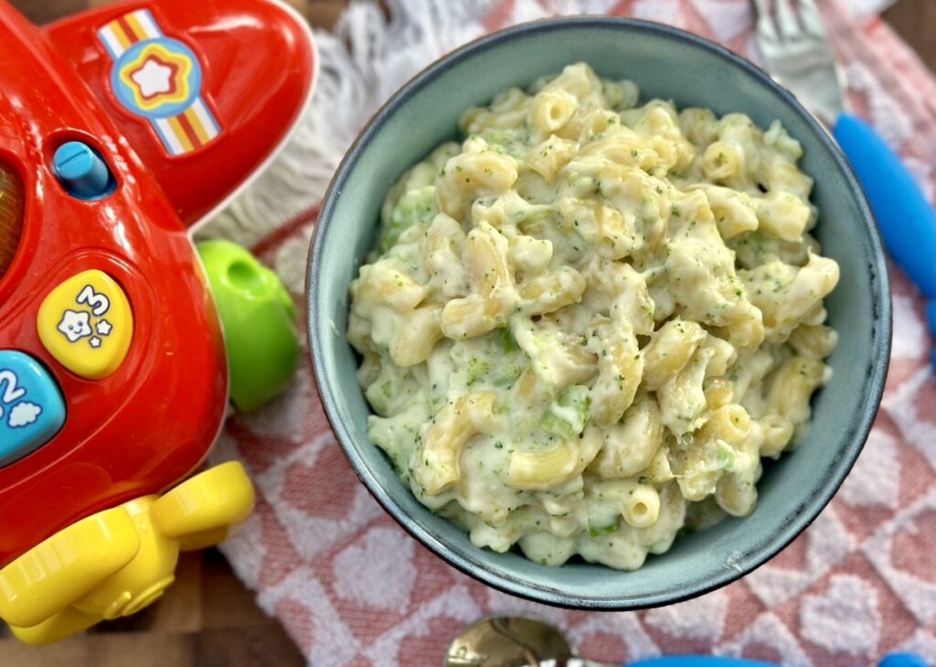 Creamy homemade mac and cheese for babies served in a blue bowl with a colourful toy airplane beside it