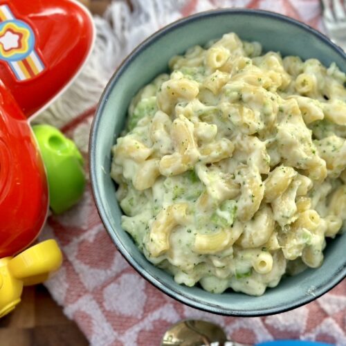 Creamy homemade mac and cheese for babies served in a blue bowl with a colourful toy airplane beside it