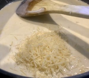 Adding grated cheese to creamy garlic sauce