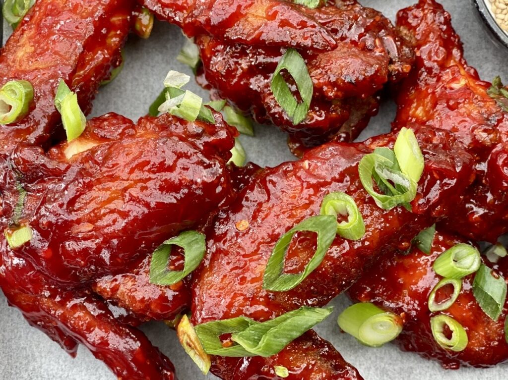 Close up of sticky Korean style chicken wings with a thick spicy red glaze, showing the glossy texture of the sauce and fresh green onion garnish.