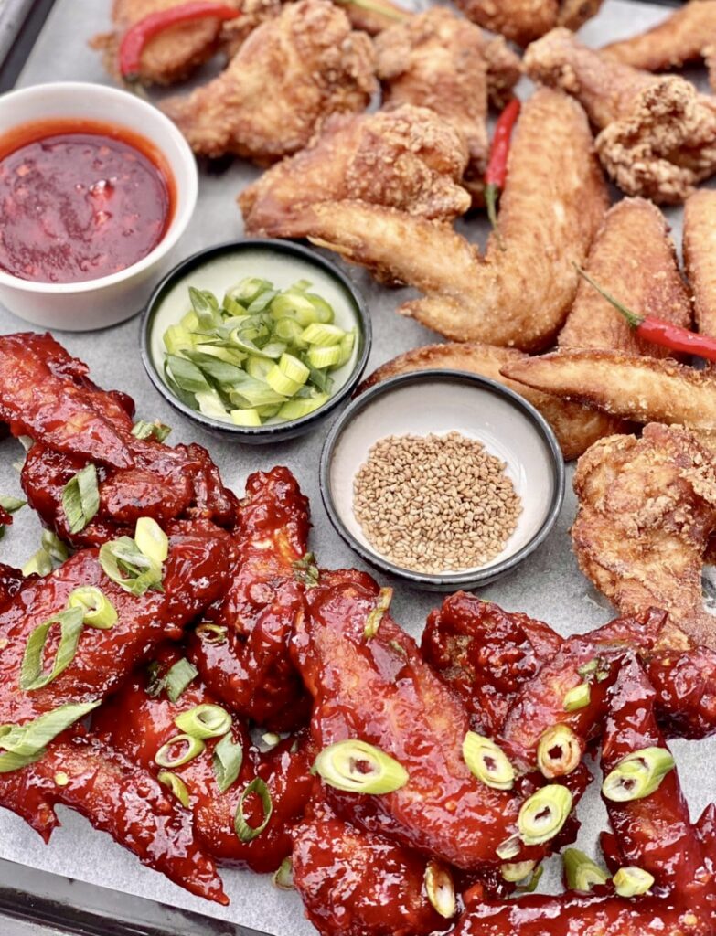 Spicy Korean chicken wings and golden crispy wings served side by side on a tray with red chilli garnish and dipping sauces.