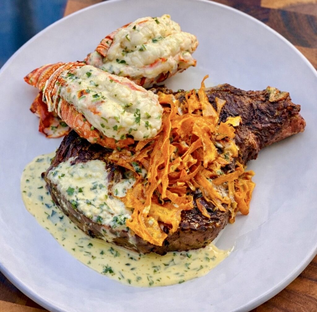 Surf and turf with lobster showing juicy grilled steak, buttered lobster tails, crispy sweet potato ribbons, and creamy herb sauce