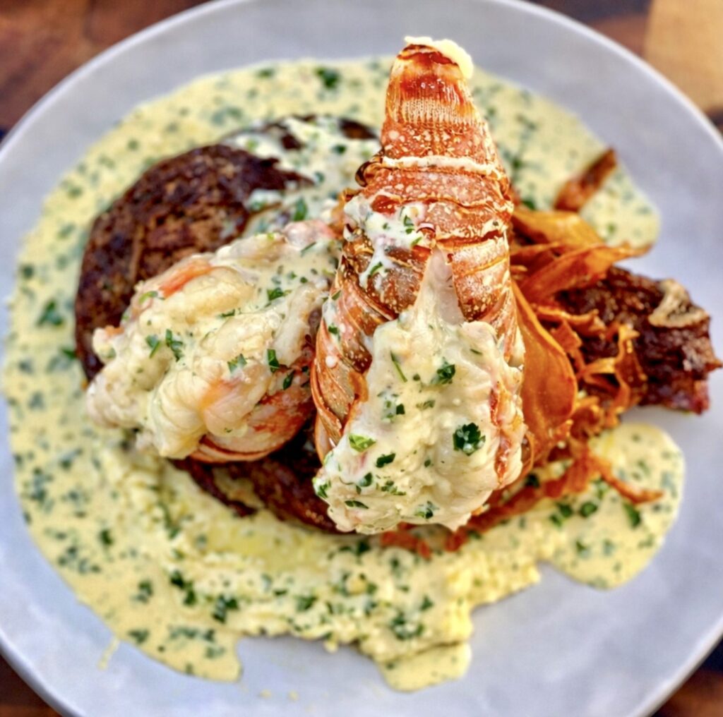 Top-down view of surf and turf with lobster served with steak, lobster tails, crispy sweet potatoes, and rich creamy herb sauce