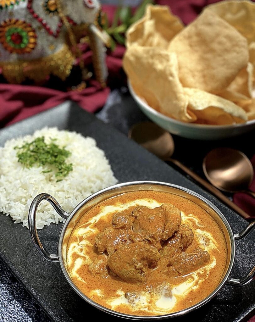Easy butter chicken served in a traditional metal curry bowl with fluffy white rice and crispy papadums on the side.
