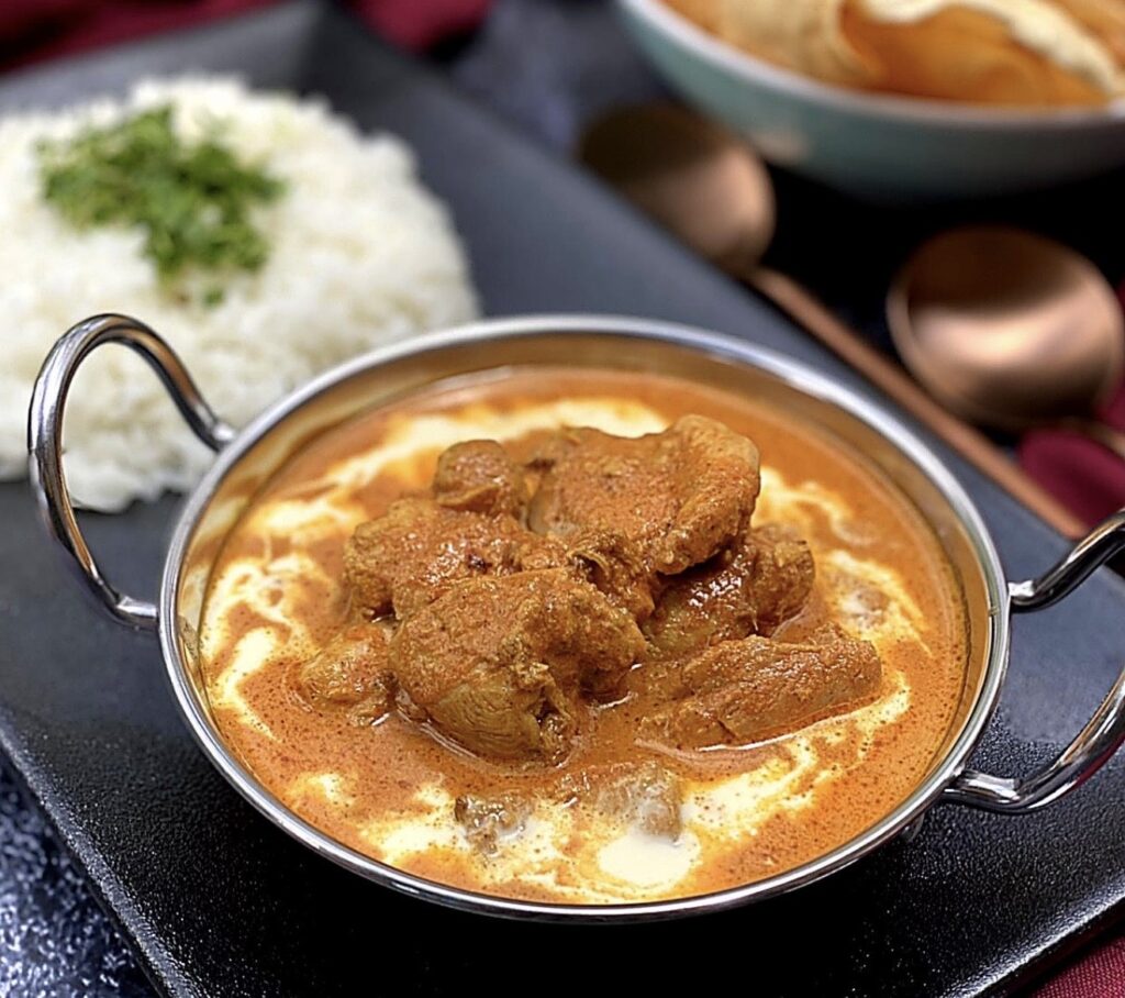 Close up of easy butter chicken in a creamy tomato sauce with tender chicken pieces and a swirl of cream.