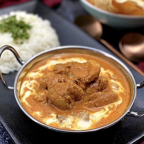 Close up of easy butter chicken in a creamy tomato sauce with tender chicken pieces and a swirl of cream.