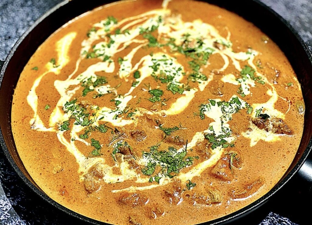 Easy butter chicken simmering in a pan, topped with cream swirl and fresh coriander for garnish.