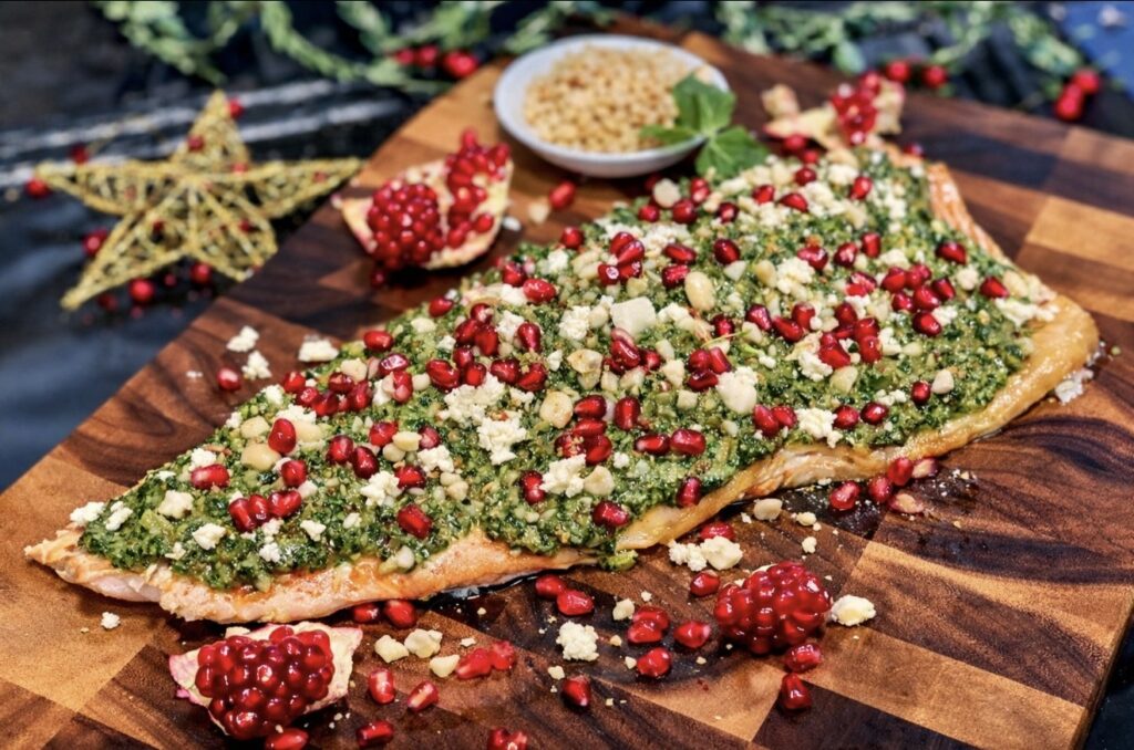 Whole oven roasted salmon with herb salsa verde, feta, macadamia nuts and pomegranate, styled as an elegant centrepiece.