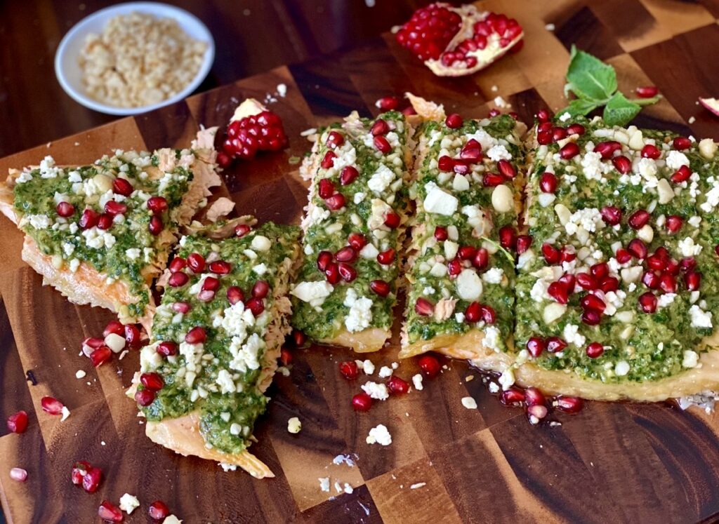 Salmon with salsa verde served on a wooden cutting board, garnished with feta, macadamia nuts and vibrant pomegranate arils.