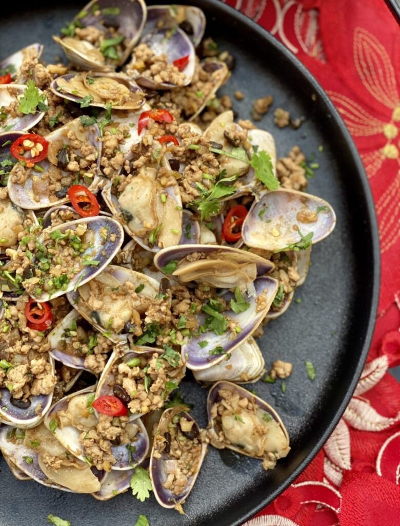 Chinese pork and clams served on a black plate, cooked with garlic, chilli, and herbs