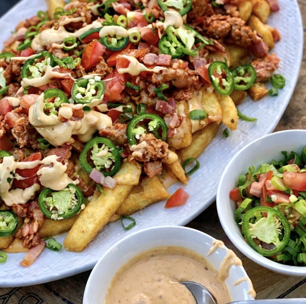 Plate of loaded fries with sausage, bacon and jalapeños served with creamy cheesy sauce and fresh tomato salsa.