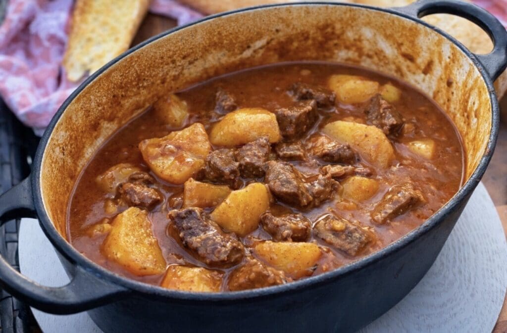 Hearty beef and potato stew simmered in a rich tomato gravy served in a cast iron pot.