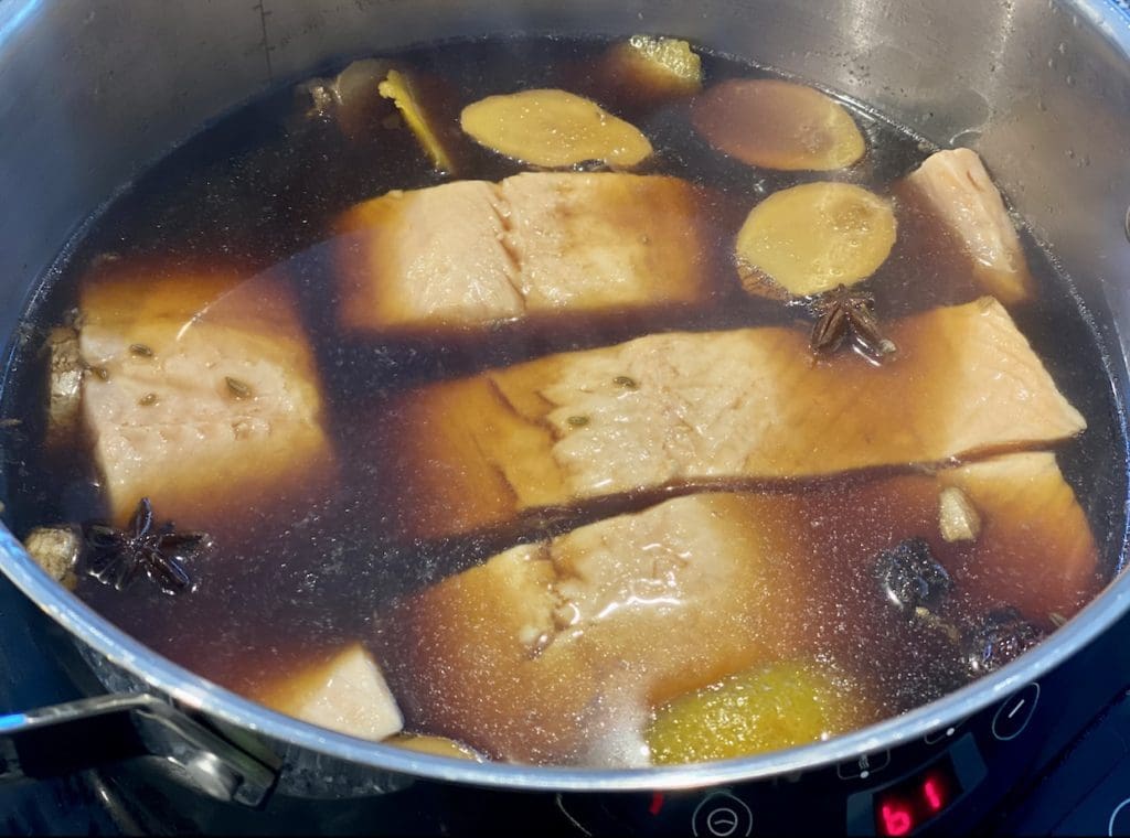 Poached Salmon in Chinese spiced broth in a saucepan, cooked with the aromatics and ready to be served