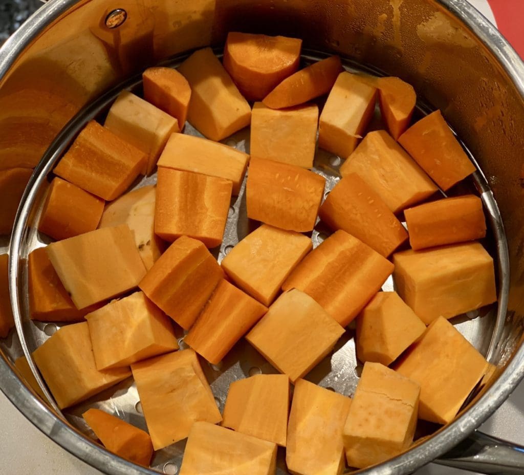 Chopped sweet potatoes and carrots in a steamer basket in one layer