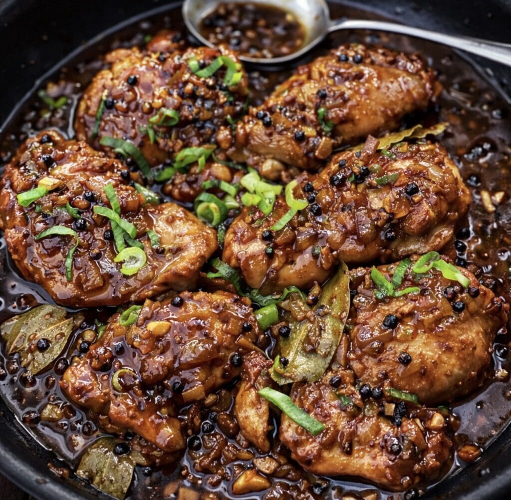 Braised chicken adobo pieces simmering in a glossy soy-vinegar sauce with garlic and spring onions