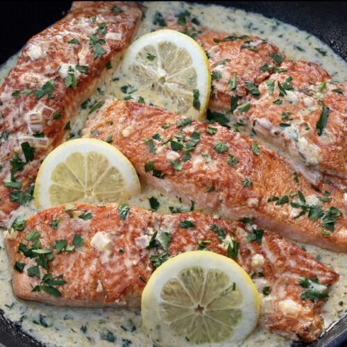 Creamy lemon salmon in a black skillet topped with fresh parsley and lemon slices.