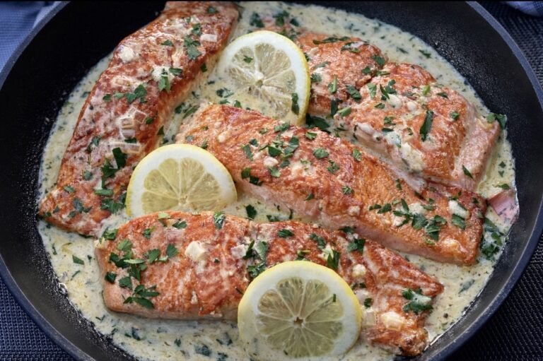 Creamy lemon salmon in a black skillet topped with fresh parsley and lemon slices.