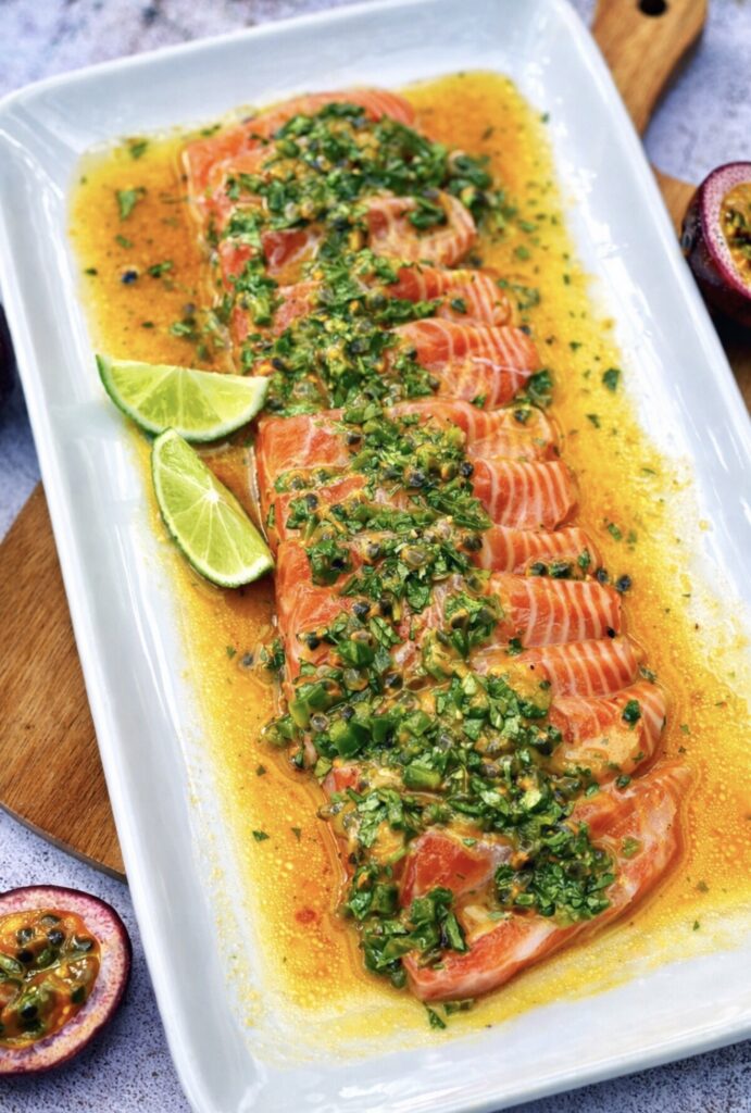 Salmon ceviche plated with passionfruit dressing, jalapeño, lime wedges and fish sauce, styled on a rectangular serving plate