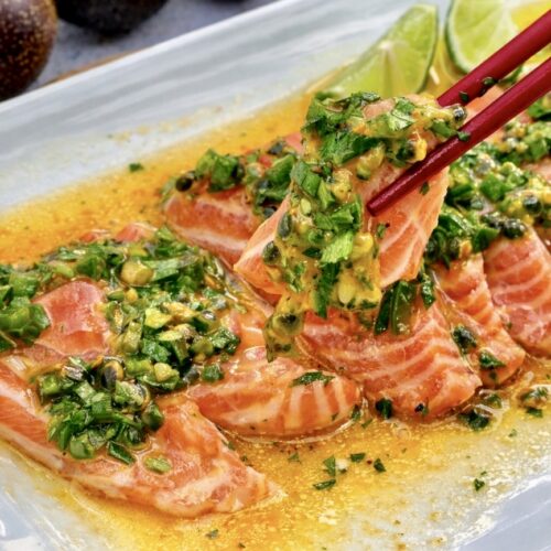 Close up of salmon ceviche with passionfruit jalapeño lime and fish sauce, showing glossy salmon slices and vibrant green herbs