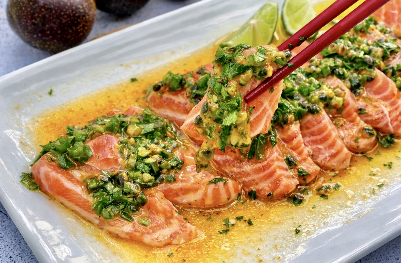 Close up of salmon ceviche with passionfruit jalapeño lime and fish sauce, showing glossy salmon slices and vibrant green herbs
