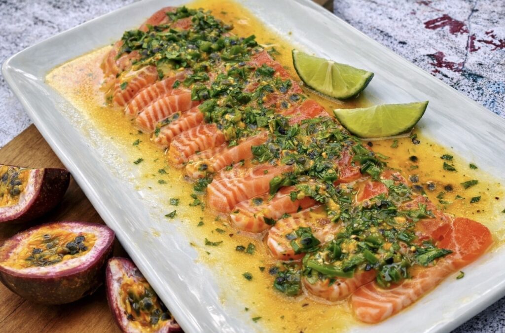 Salmon ceviche served on a white platter with passionfruit, jalapeño, lime and fish sauce, topped with fresh herbs and golden citrus dressing