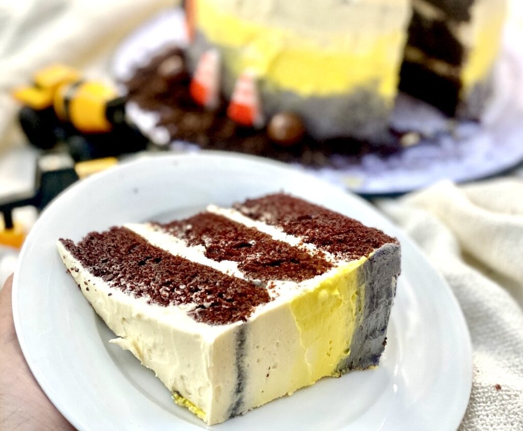 Slice of construction cake showing moist chocolate layers with vanilla buttercream and yellow and grey frosting details.