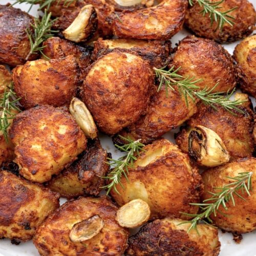 Crispy duck fat potatoes served in a white bowl with roasted garlic and fresh rosemary, perfectly golden and crunchy.