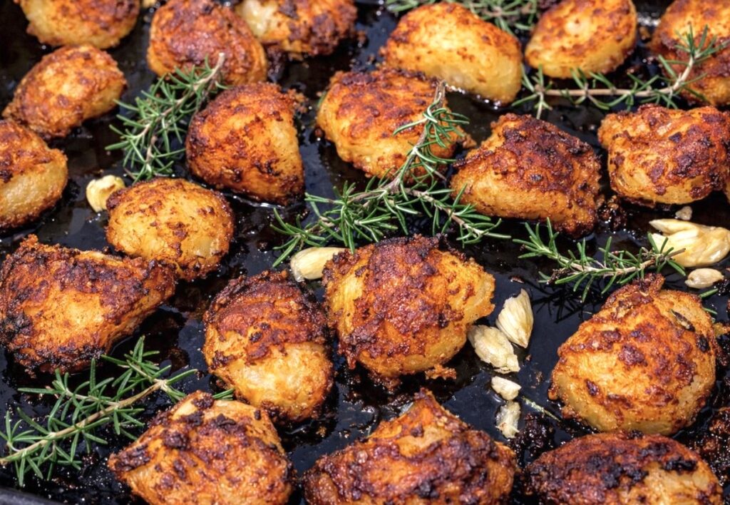 Oven roasted crispy duck fat potatoes on a black tray with rosemary and garlic, fluffy inside and ultra crunchy outside.