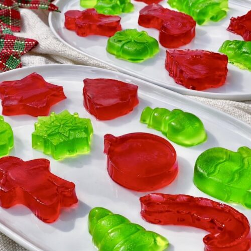 Holiday finger jello assortment in red and green, set on white serving platters for a festive dessert display