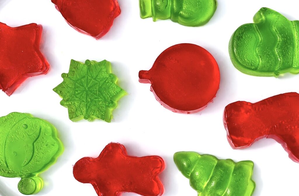 Assorted red and green finger jello treats in Christmas shapes displayed on a bright white background.