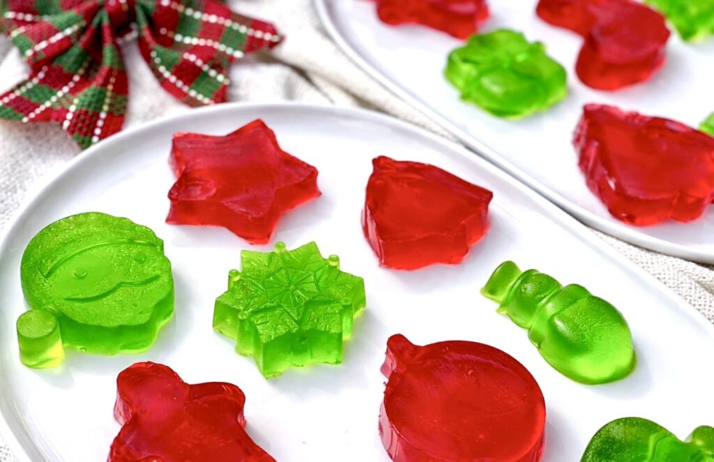 Festive red and green finger jello candies in Christmas shapes arranged on a white platter with a holiday ribbon.