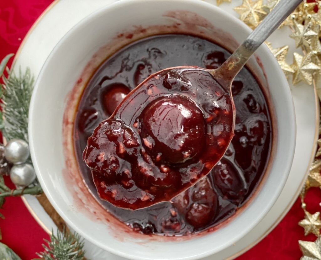 Savoury cherry sauce with whole cherries spooned from a bowl, perfect for duck, turkey or roasted meats
