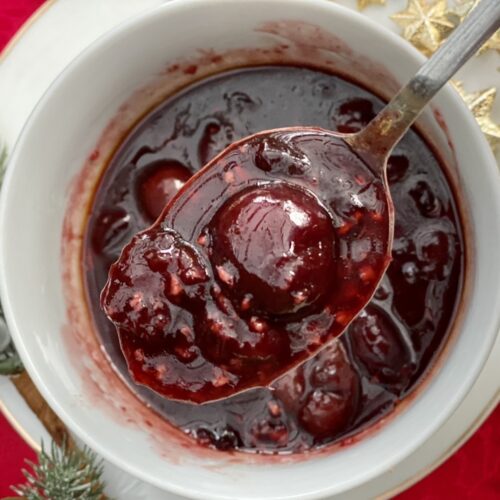 Savoury cherry sauce with whole cherries spooned from a bowl, perfect for duck, turkey or roasted meats
