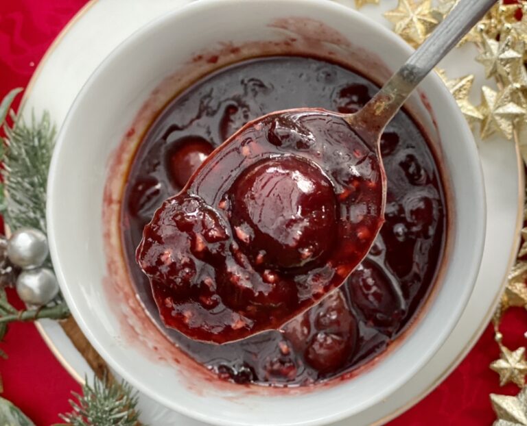 Savoury cherry sauce with whole cherries spooned from a bowl, perfect for duck, turkey or roasted meats