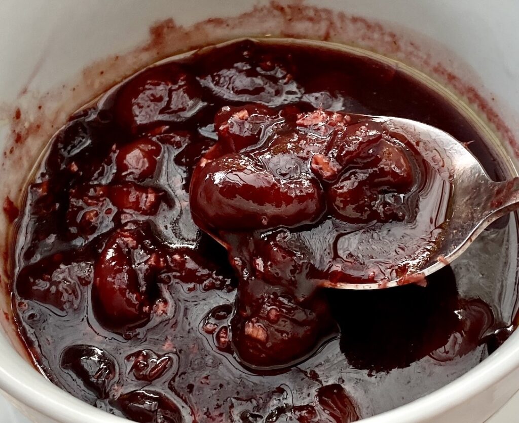 Thick savoury cherry sauce with whole cherries in a bowl, glossy and rich for roasted meats