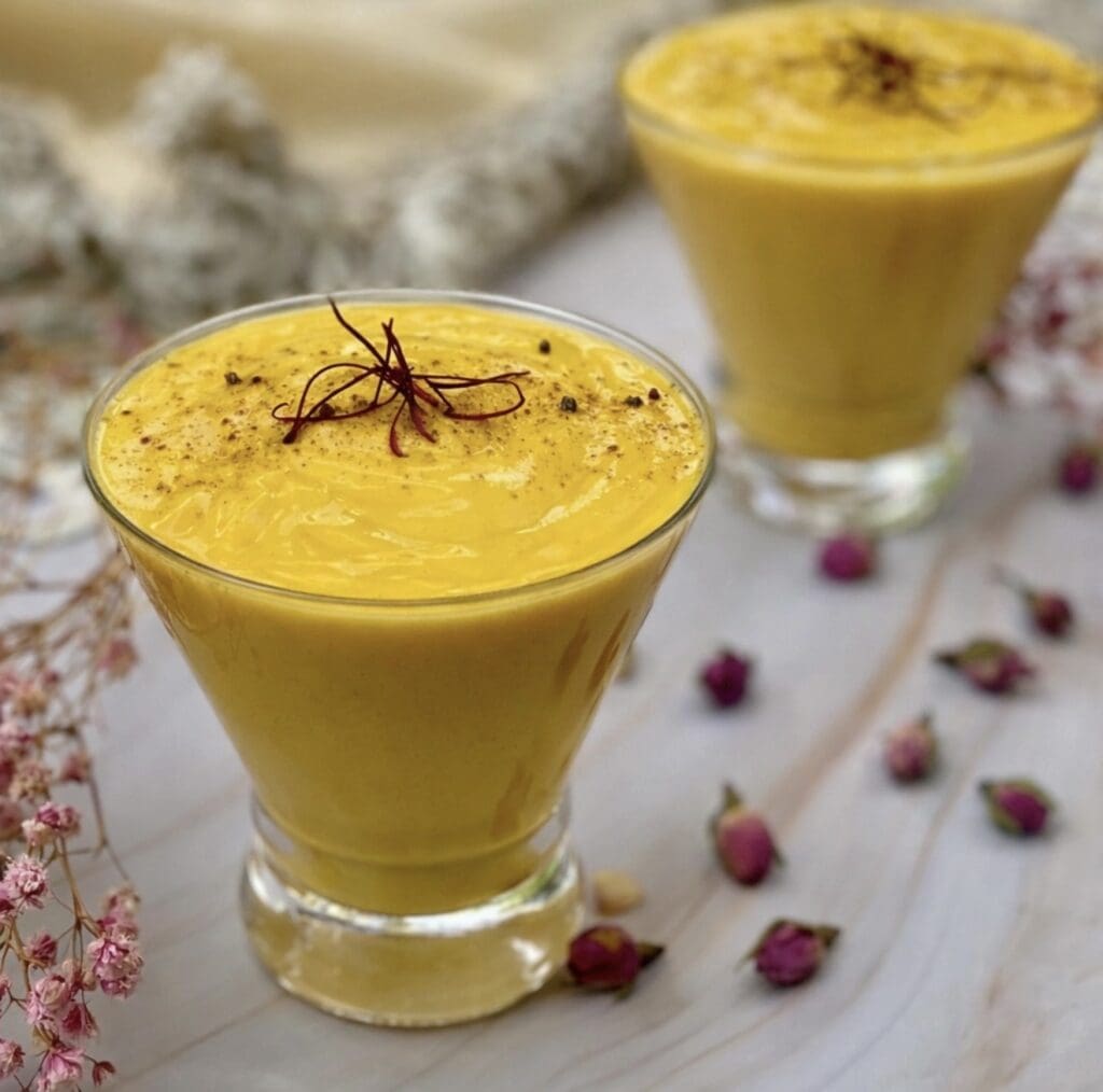 Two glasses of creamy mango lassi cocktail garnished with saffron threads