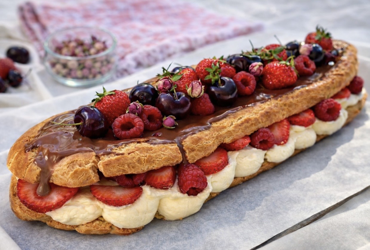 Giant chocolate éclair with fresh berries and vanilla cream, served on parchment paper with a soft linen background.
