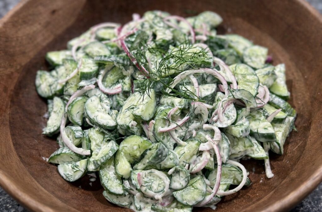 Creamy Cucumber Salad served in a wooden bowl with sliced cucumbers, red onion and fresh dill