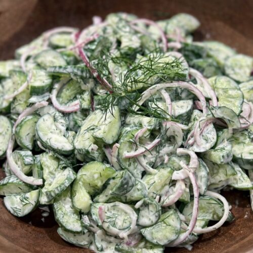 Creamy Cucumber Salad served in a wooden bowl with sliced cucumbers, red onion and fresh dill