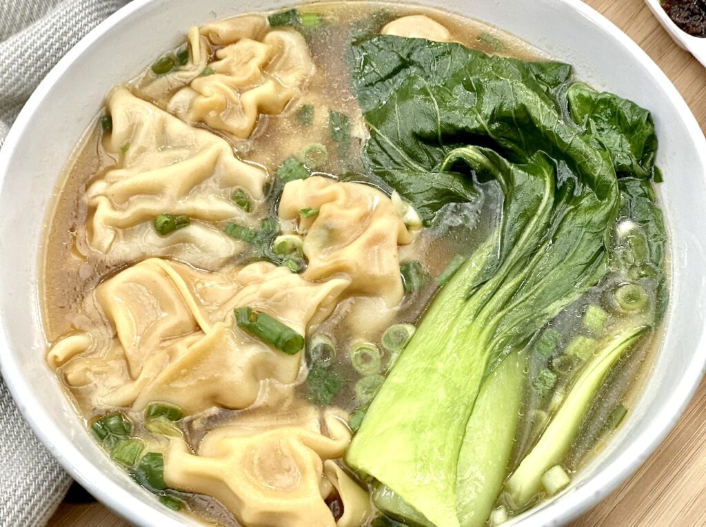 Close up of Kimchi dumplings in a bowl of simple soup and bok choy