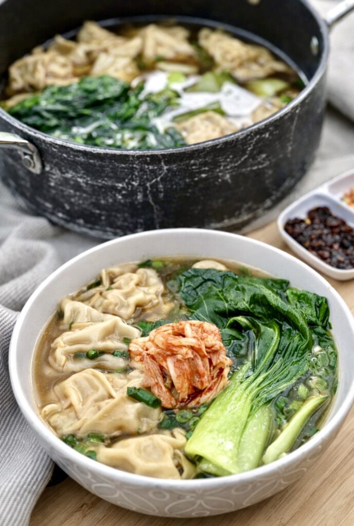 A pot and bowl filled with Kimchi dumplings with simple soup and bok choy